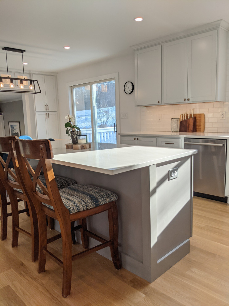 Inspiration for a mid-sized transitional l-shaped light wood floor and brown floor open concept kitchen remodel in Baltimore with an undermount sink, shaker cabinets, white cabinets, quartzite countertops, white backsplash, subway tile backsplash, stainless steel appliances, an island and white countertops