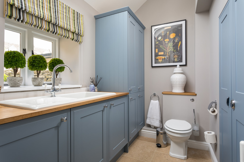 Inspiration for a small country powder room in Gloucestershire with recessed-panel cabinets, blue cabinets, a one-piece toilet, grey walls, a drop-in sink, wood benchtops, brown floor and brown benchtops.