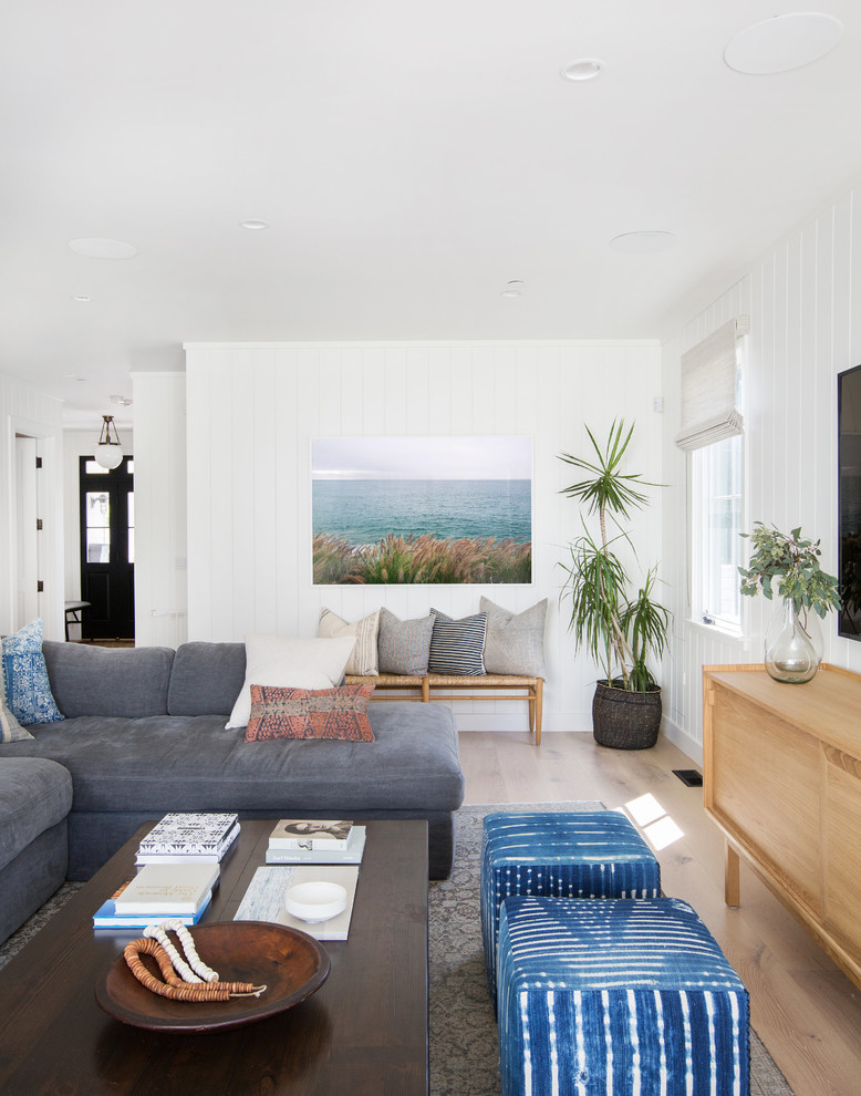 Photo of a beach style living room in San Diego with white walls, light hardwood floors, no fireplace, a wall-mounted tv and brown floor.