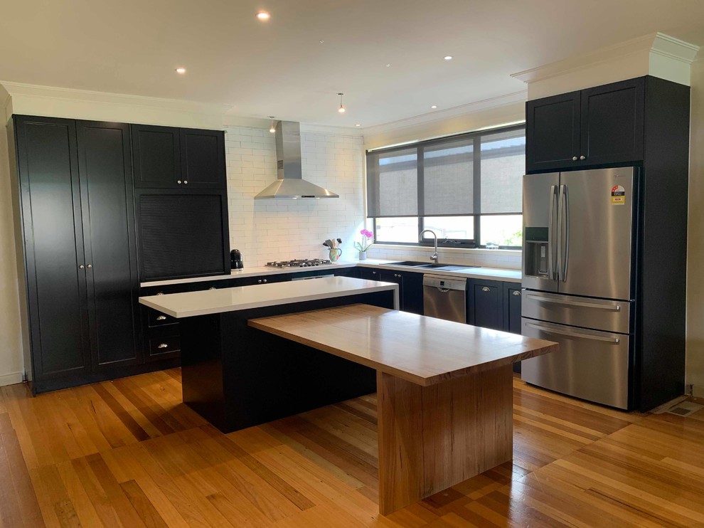 Inspiration for a large contemporary l-shaped open plan kitchen in Melbourne with shaker cabinets, with island, a double-bowl sink, black cabinets, granite benchtops, white splashback, porcelain splashback, stainless steel appliances, white benchtop and medium hardwood floors.