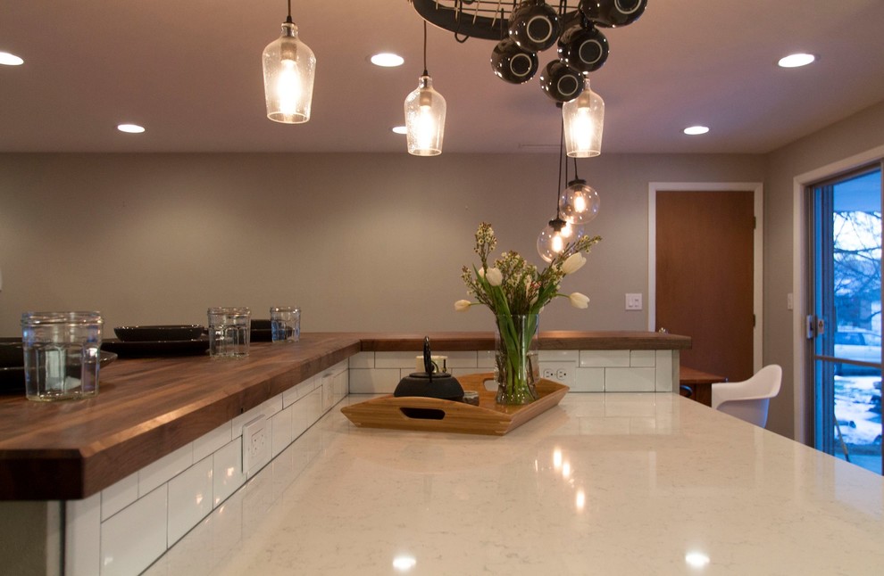Eat-in kitchen - mid-sized transitional l-shaped medium tone wood floor eat-in kitchen idea in Denver with a farmhouse sink, shaker cabinets, gray cabinets, quartz countertops, white backsplash, ceramic backsplash, stainless steel appliances and an island