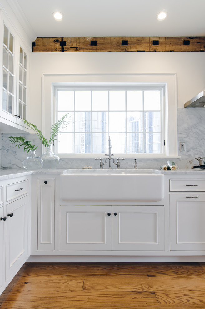 Photo of a large country u-shaped eat-in kitchen in New York with a farmhouse sink, beaded inset cabinets, white cabinets, white splashback, stainless steel appliances, medium hardwood floors, with island and marble benchtops.