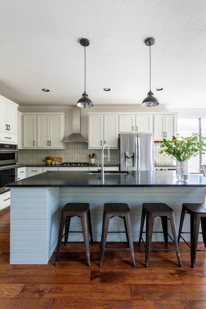 Inspiration for a mid-sized transitional l-shaped medium tone wood floor and brown floor eat-in kitchen remodel in Austin with an undermount sink, shaker cabinets, white cabinets, soapstone countertops, beige backsplash, ceramic backsplash, stainless steel appliances, an island and black countertops