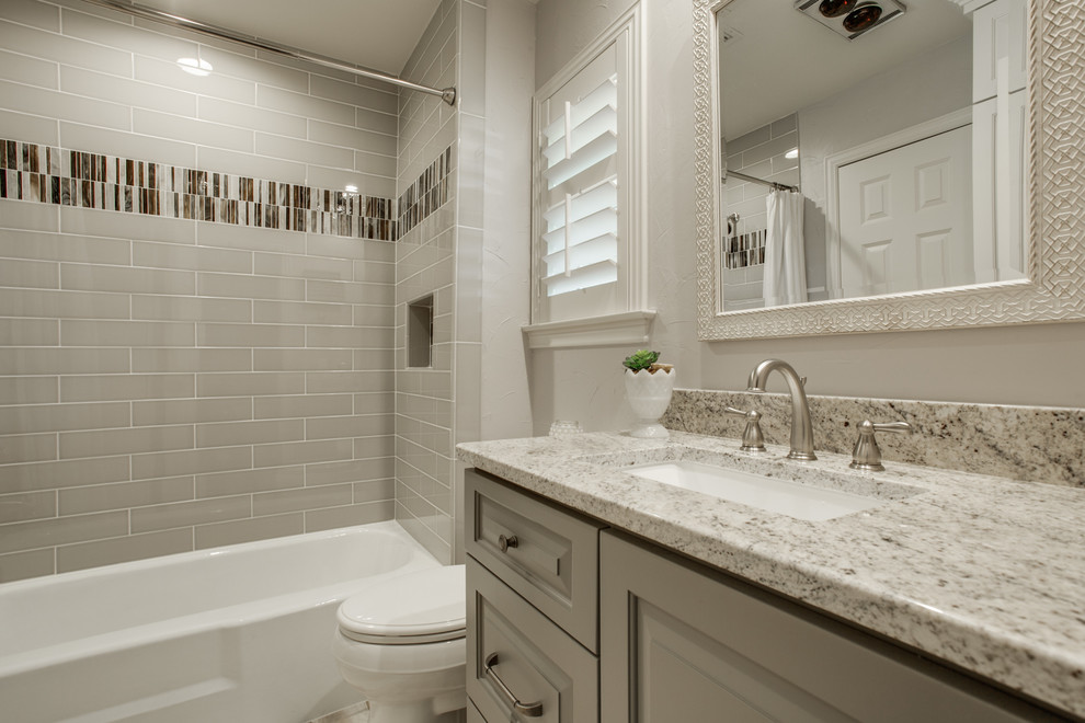 This is an example of a mid-sized traditional 3/4 bathroom in Dallas with raised-panel cabinets, grey cabinets, an alcove tub, a shower/bathtub combo, a one-piece toilet, beige tile, ceramic tile, beige walls, an undermount sink, quartzite benchtops and a shower curtain.