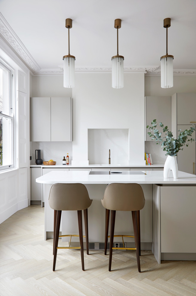This is an example of a large contemporary grey and cream open plan kitchen in London with a belfast sink, flat-panel cabinets, grey cabinets, granite worktops, white splashback, granite splashback, integrated appliances, light hardwood flooring, an island, brown floors and white worktops.