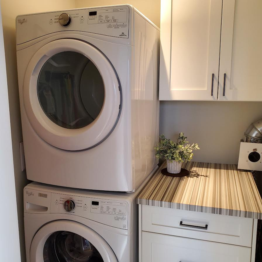 Inspiration for a small modern single-wall dedicated laundry room in Vancouver with shaker cabinets, white cabinets, laminate benchtops, green walls, ceramic floors, a stacked washer and dryer, grey floor and multi-coloured benchtop.