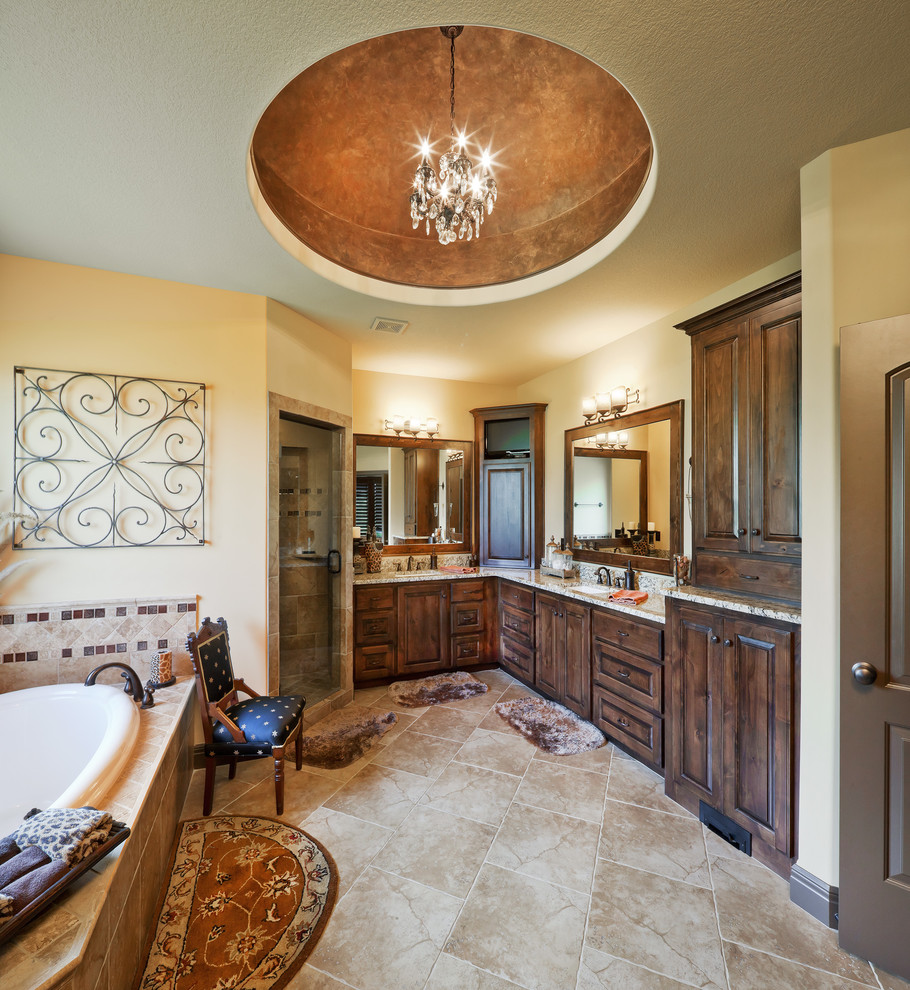 Photo of a large mediterranean bathroom in Kansas City with raised-panel cabinets, dark wood cabinets, a drop-in tub, beige tile and beige walls.