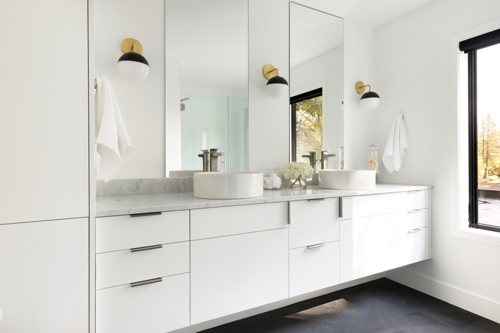 Modelo de cuarto de baño doble y flotante contemporáneo con armarios con paneles lisos, puertas de armario blancas, paredes blancas, lavabo sobreencimera, suelo negro y encimeras blancas