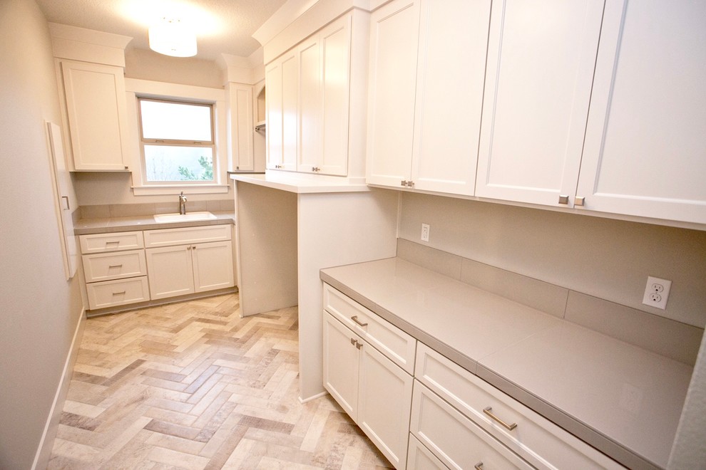 Inspiration for a large traditional galley dedicated laundry room in Portland with a drop-in sink, shaker cabinets, white cabinets, tile benchtops, grey walls, porcelain floors and a side-by-side washer and dryer.