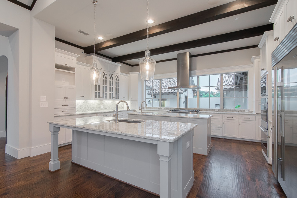 This is an example of a large mediterranean u-shaped eat-in kitchen in Dallas with an undermount sink, white cabinets, granite benchtops, white splashback, stone slab splashback, stainless steel appliances, medium hardwood floors, multiple islands, brown floor and shaker cabinets.