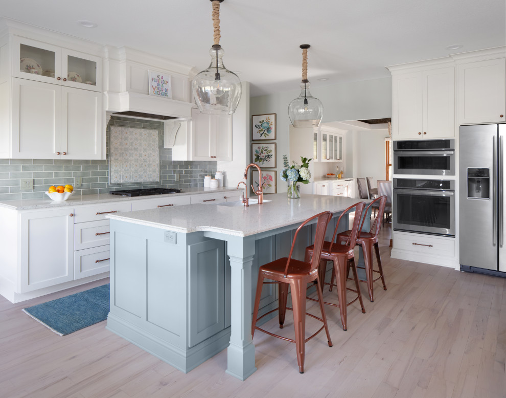 Country l-shaped eat-in kitchen in Milwaukee with a farmhouse sink, shaker cabinets, white cabinets, quartz benchtops, green splashback, ceramic splashback, stainless steel appliances, light hardwood floors, with island, white floor and white benchtop.