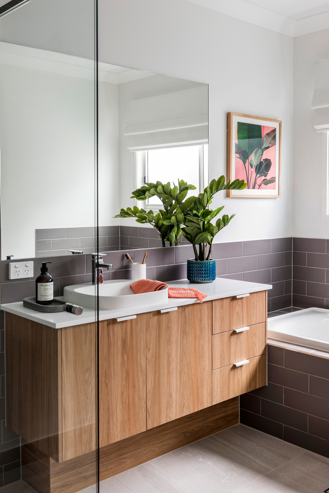 Photo of a beach style 3/4 bathroom in Gold Coast - Tweed with flat-panel cabinets, medium wood cabinets, a drop-in tub, brown tile, white walls, a drop-in sink, beige floor and white benchtops.