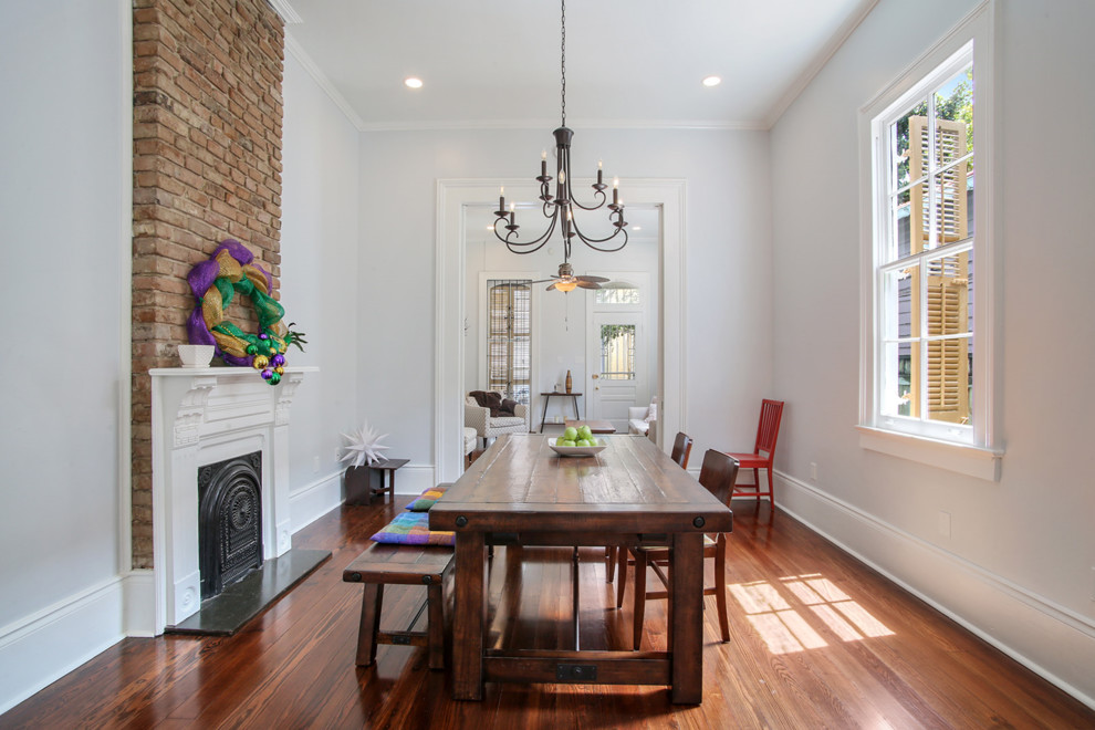 Small traditional separate dining room in New Orleans with white walls, medium hardwood floors, a standard fireplace, a plaster fireplace surround and brown floor.