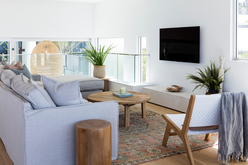 Inspiration for a contemporary loft-style living room in Sunshine Coast with white walls, medium hardwood floors, a wall-mounted tv and brown floor.