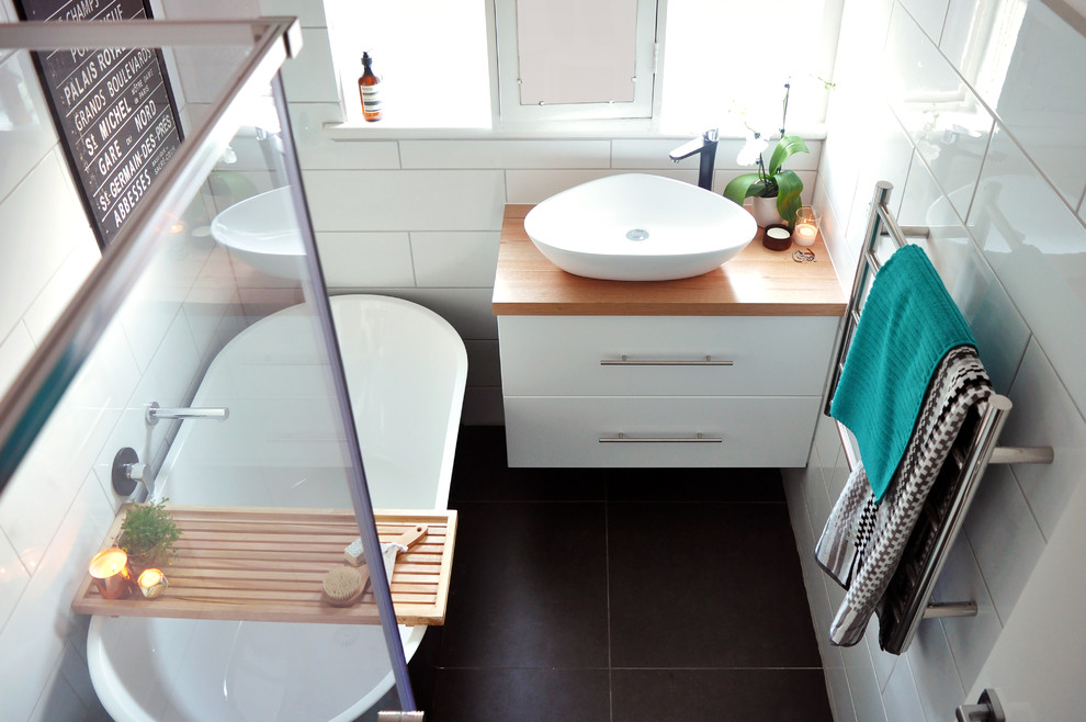 This is an example of a small contemporary master bathroom in Melbourne with white cabinets, a freestanding tub, a corner shower, black and white tile, ceramic tile, white walls, ceramic floors, a vessel sink and wood benchtops.