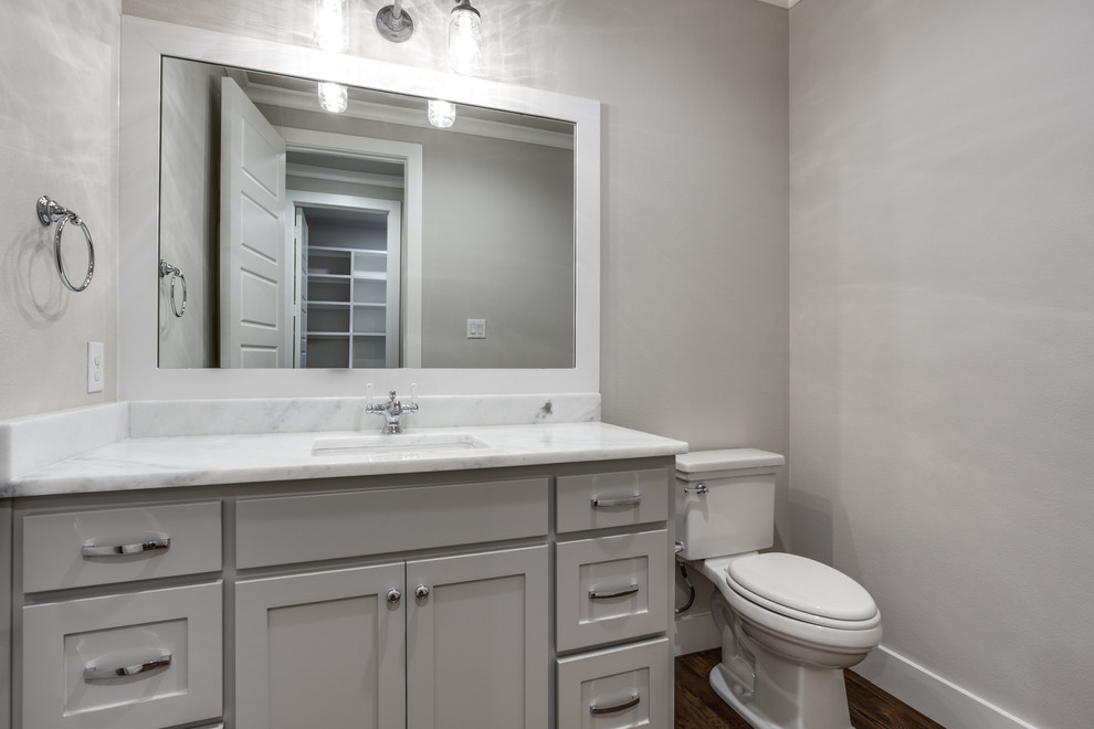 Photo of a mid-sized transitional 3/4 bathroom in Dallas with shaker cabinets, grey cabinets, a two-piece toilet, white tile, subway tile, an undermount sink, marble benchtops, dark hardwood floors and grey walls.