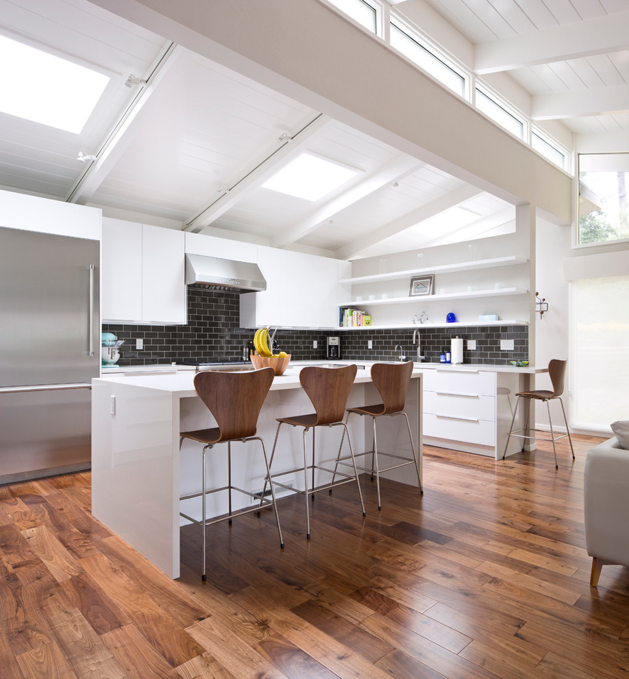 Photo of a large midcentury l-shaped eat-in kitchen in San Francisco with an undermount sink, flat-panel cabinets, white cabinets, quartz benchtops, black splashback, subway tile splashback, stainless steel appliances, dark hardwood floors, with island and brown floor.