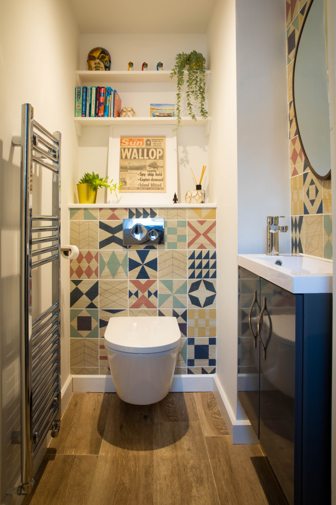 This is an example of a small eclectic cloakroom in Kent with flat-panel cabinets, blue cabinets, a wall mounted toilet, multi-coloured tiles, porcelain tiles, white walls, porcelain flooring, an integrated sink, quartz worktops, beige floors, white worktops, a feature wall and a floating vanity unit.