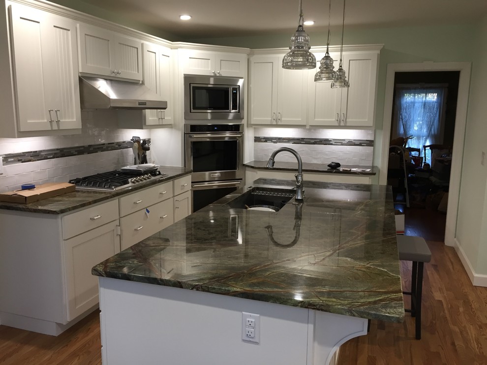 Kitchen - mid-sized transitional l-shaped medium tone wood floor and brown floor kitchen idea in Atlanta with a farmhouse sink, shaker cabinets, white cabinets, marble countertops, white backsplash, ceramic backsplash, stainless steel appliances and an island