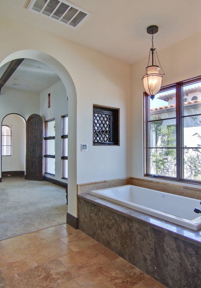 Photo of a mediterranean bathroom in Los Angeles with a drop-in tub, granite benchtops, beige tile and stone tile.