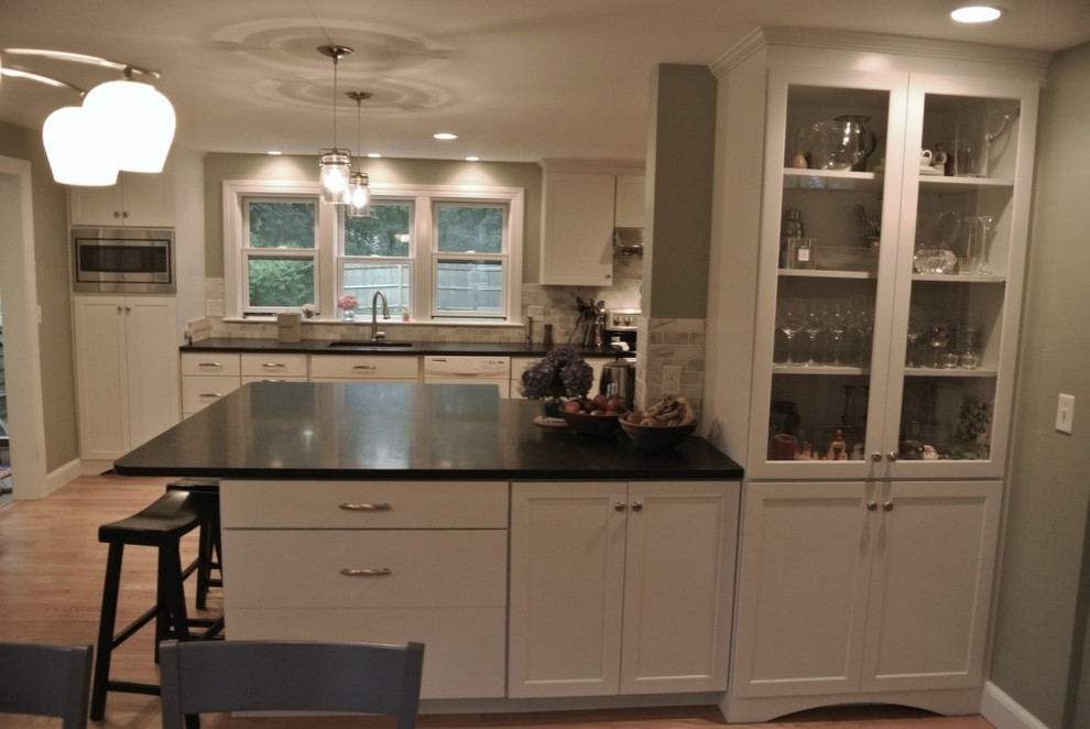 Example of a transitional u-shaped light wood floor eat-in kitchen design in Boston with an undermount sink, shaker cabinets, white cabinets, beige backsplash, porcelain backsplash, stainless steel appliances, a peninsula and black countertops