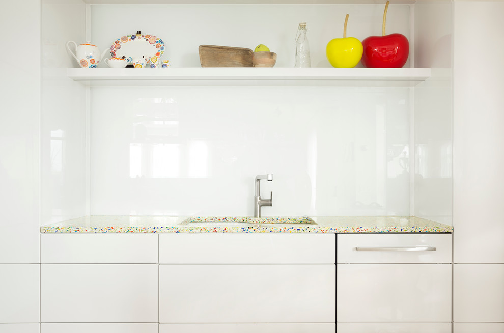 Inspiration for a mid-sized contemporary galley separate kitchen in Montreal with an undermount sink, flat-panel cabinets, white cabinets, recycled glass benchtops, white splashback, glass sheet splashback, white appliances, light hardwood floors and no island.