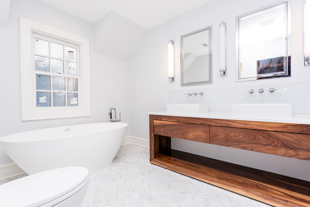 Inspiration for a contemporary master bathroom in St Louis with open cabinets, medium wood cabinets, a freestanding tub, white tile, subway tile, grey walls, mosaic tile floors, a vessel sink and marble benchtops.