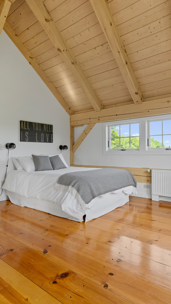 Large country guest bedroom in New York with white walls, medium hardwood floors and exposed beam.