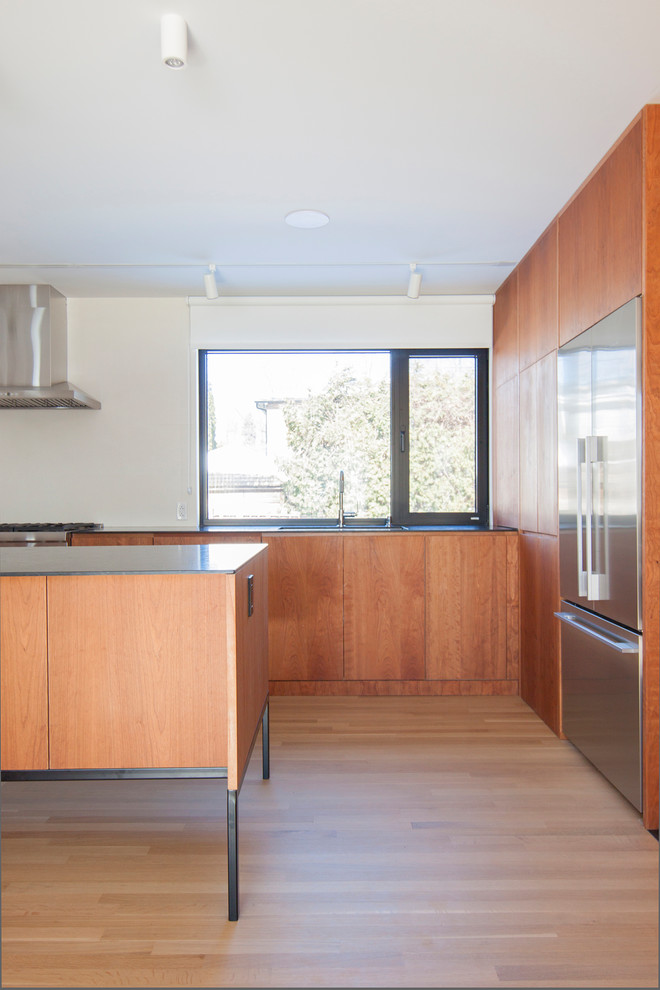 Inspiration for a mid-sized modern l-shaped open plan kitchen in Montreal with a double-bowl sink, flat-panel cabinets, medium wood cabinets, granite benchtops, white splashback, ceramic splashback, stainless steel appliances, light hardwood floors, with island and black benchtop.