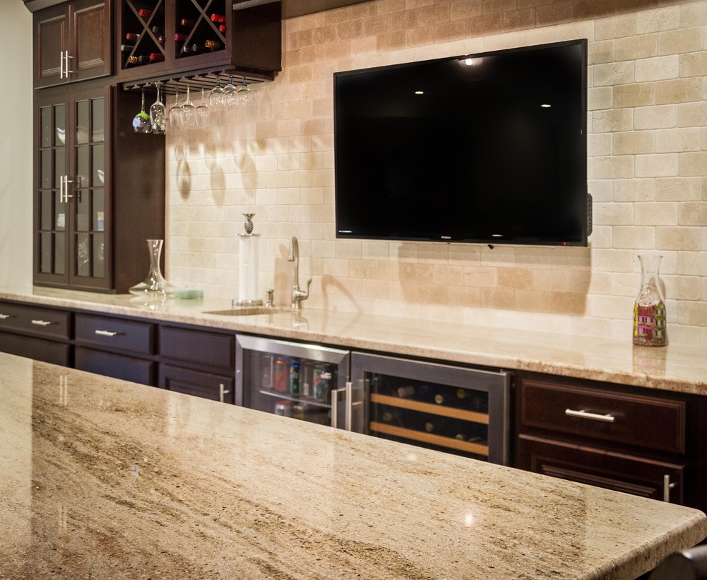 This is an example of a mid-sized transitional galley seated home bar in DC Metro with an undermount sink, raised-panel cabinets, dark wood cabinets, granite benchtops, beige splashback and subway tile splashback.