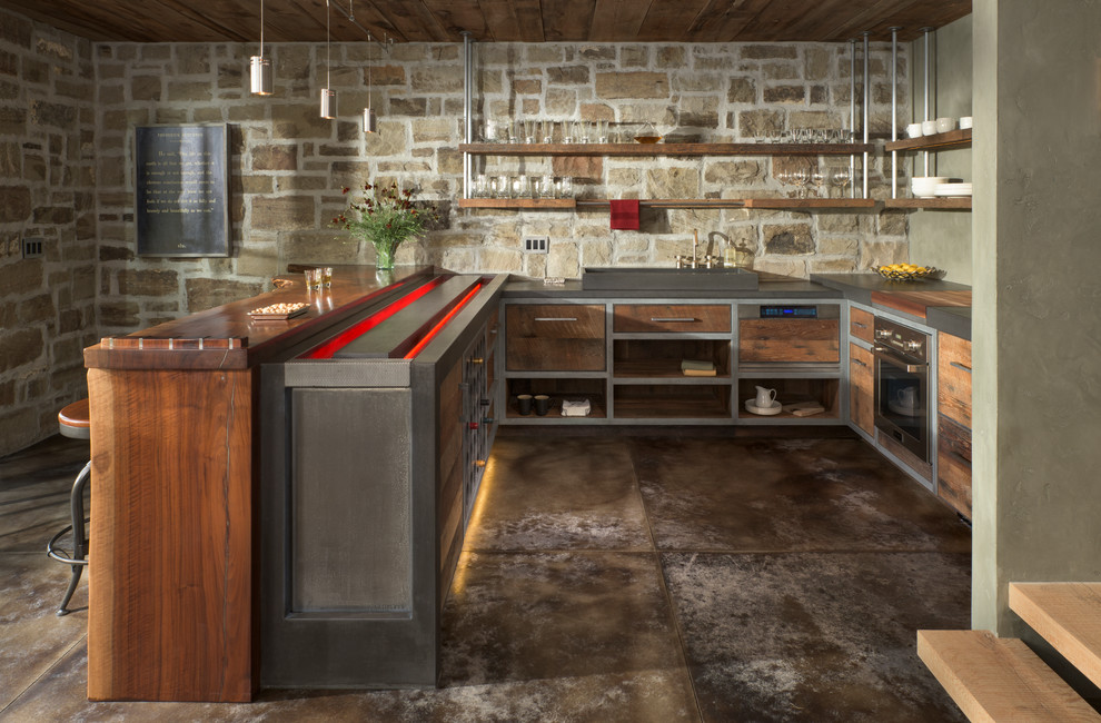 This is an example of a mid-sized country u-shaped open plan kitchen in Other with a single-bowl sink, flat-panel cabinets, medium wood cabinets, concrete benchtops, grey splashback, panelled appliances and concrete floors.