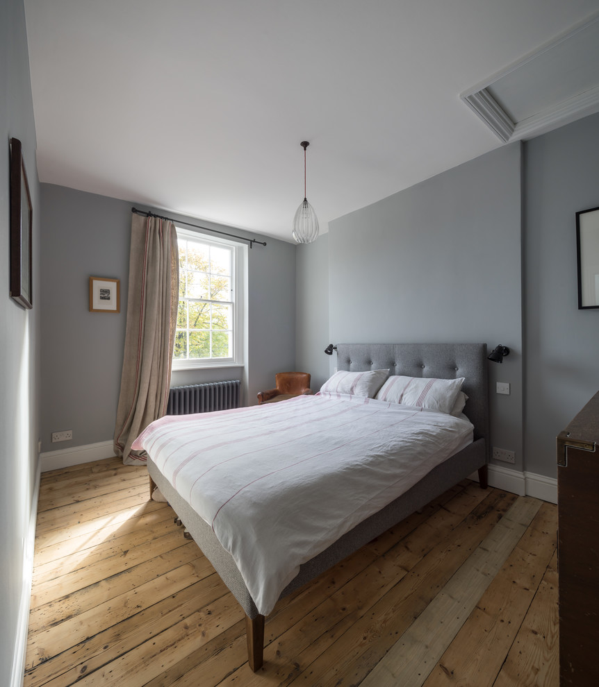 This is an example of a mid-sized transitional master bedroom in London with grey walls and medium hardwood floors.