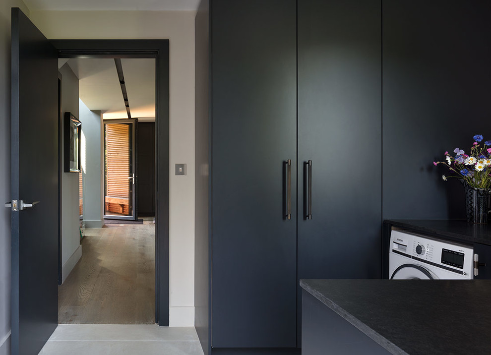 This is an example of a large contemporary single-wall utility room in London with an undermount sink, marble benchtops, light hardwood floors, grey cabinets, flat-panel cabinets, grey walls, an integrated washer and dryer and black benchtop.