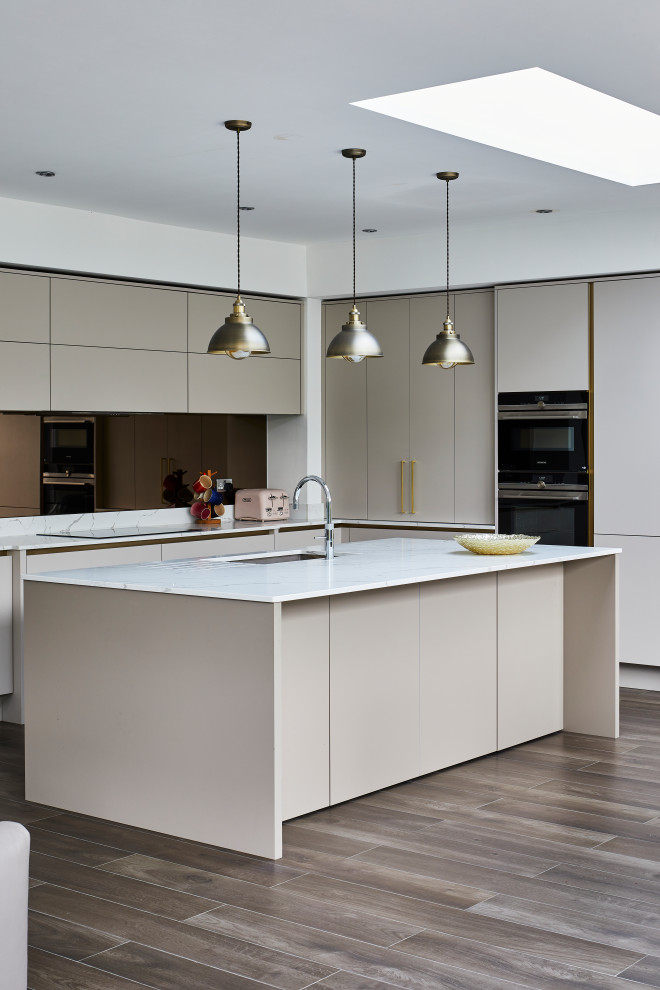 Mid-sized contemporary u-shaped open plan kitchen in London with a drop-in sink, flat-panel cabinets, beige cabinets, marble benchtops, white splashback, marble splashback, black appliances, medium hardwood floors, with island, brown floor and white benchtop.