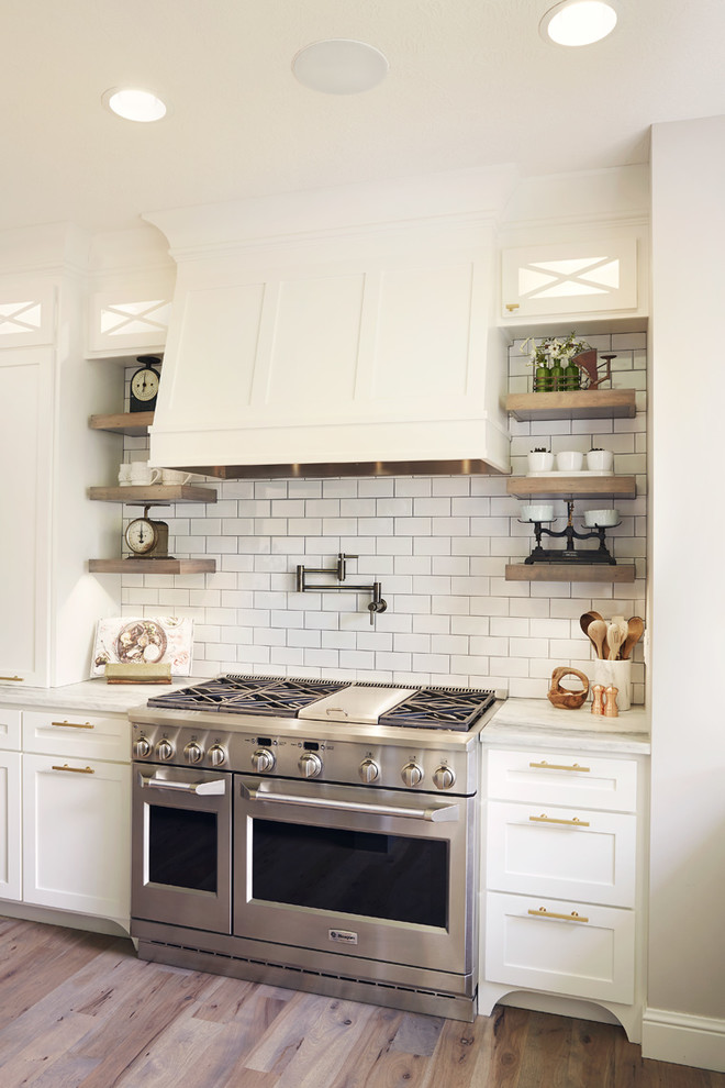 Eat-in kitchen - huge rustic l-shaped medium tone wood floor eat-in kitchen idea with a farmhouse sink, shaker cabinets, white cabinets, white backsplash, subway tile backsplash, stainless steel appliances, an island and white countertops