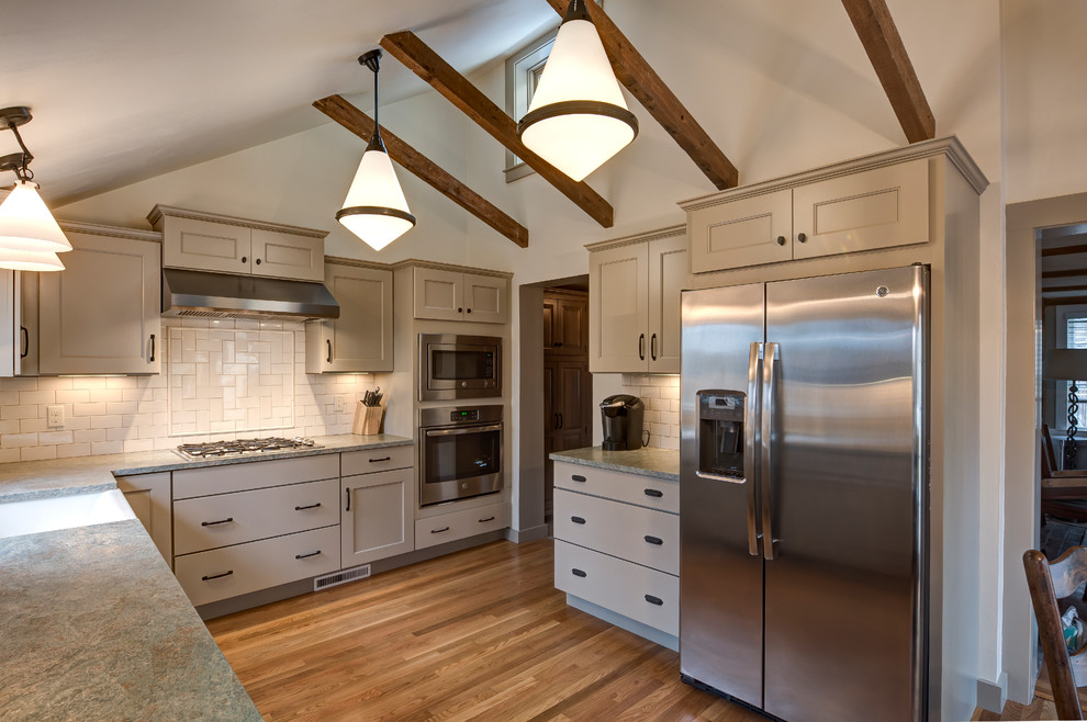 Design ideas for a mid-sized traditional l-shaped kitchen pantry in Boston with a farmhouse sink, recessed-panel cabinets, beige cabinets, granite benchtops, beige splashback, subway tile splashback, stainless steel appliances, medium hardwood floors, no island and brown floor.