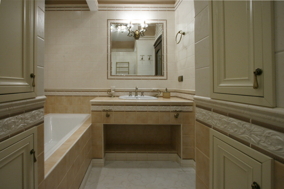 Photo of a medium sized traditional cloakroom in Moscow with raised-panel cabinets, beige cabinets, a wall mounted toilet, beige tiles, ceramic tiles, beige walls, ceramic flooring, a submerged sink, tiled worktops, beige floors, beige worktops and a freestanding vanity unit.