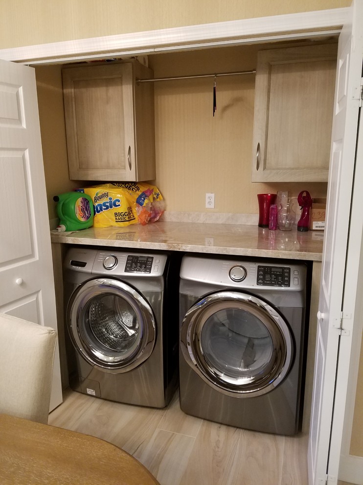 This is an example of a mid-sized transitional single-wall laundry cupboard in Miami with light wood cabinets, granite benchtops, porcelain floors, a side-by-side washer and dryer and recessed-panel cabinets.