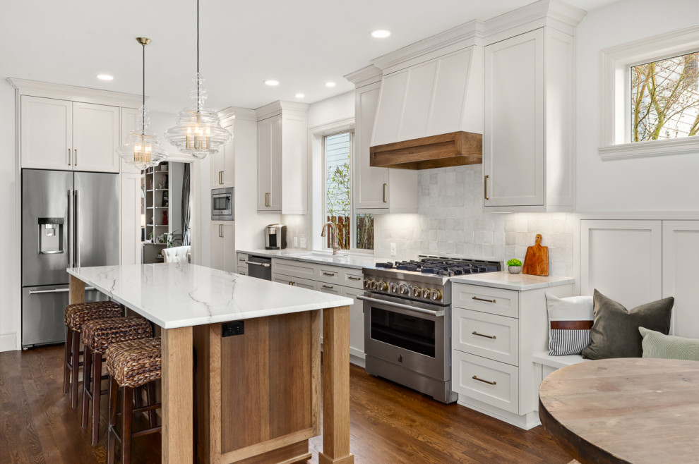 Transitional l-shaped open plan kitchen in Portland with an undermount sink, shaker cabinets, white cabinets, quartzite benchtops, white splashback, terra-cotta splashback, stainless steel appliances, medium hardwood floors, with island, brown floor and white benchtop.