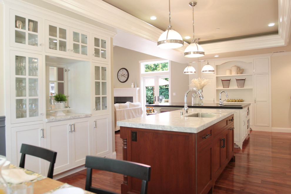 This is an example of a traditional open plan kitchen in San Francisco with glass-front cabinets and white cabinets.