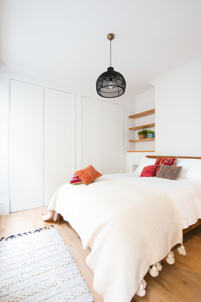 This is an example of a mid-sized mediterranean guest bedroom in London with white walls, light hardwood floors, beige floor and no fireplace.