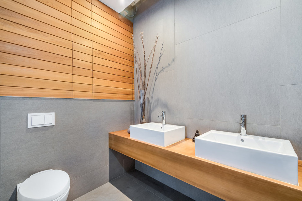Inspiration for a modern wet room bathroom in New York with a wall-mount toilet, porcelain tile, porcelain floors, a vessel sink, wood benchtops and grey floor.