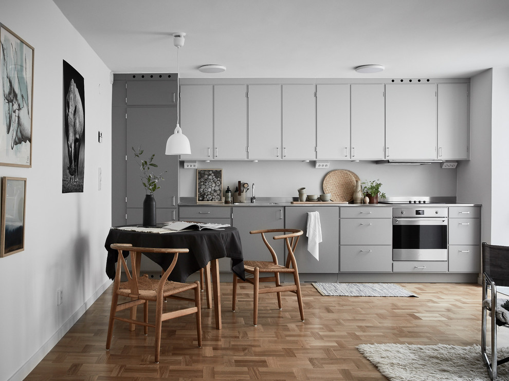 Photo of a scandinavian single-wall eat-in kitchen in Stockholm with flat-panel cabinets, grey cabinets, grey splashback, stainless steel appliances, medium hardwood floors and brown floor.