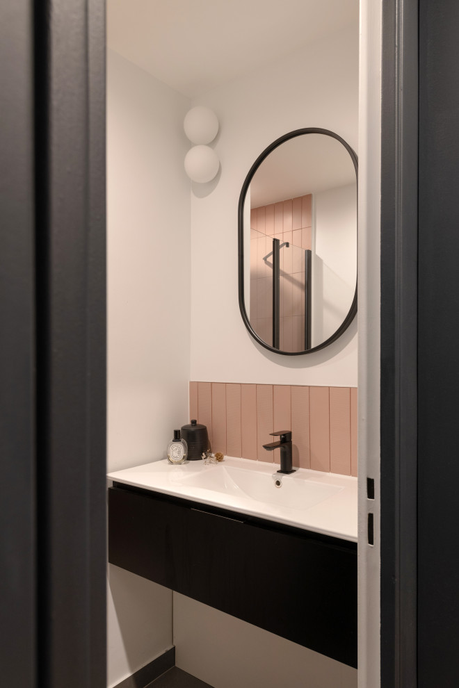 Mid-sized modern 3/4 bathroom in Lyon with black cabinets, a curbless shower, pink tile, solid surface benchtops, a hinged shower door, a single vanity, a floating vanity, flat-panel cabinets, a two-piece toilet, ceramic tile, white walls, ceramic floors, a wall-mount sink, grey floor and white benchtops.