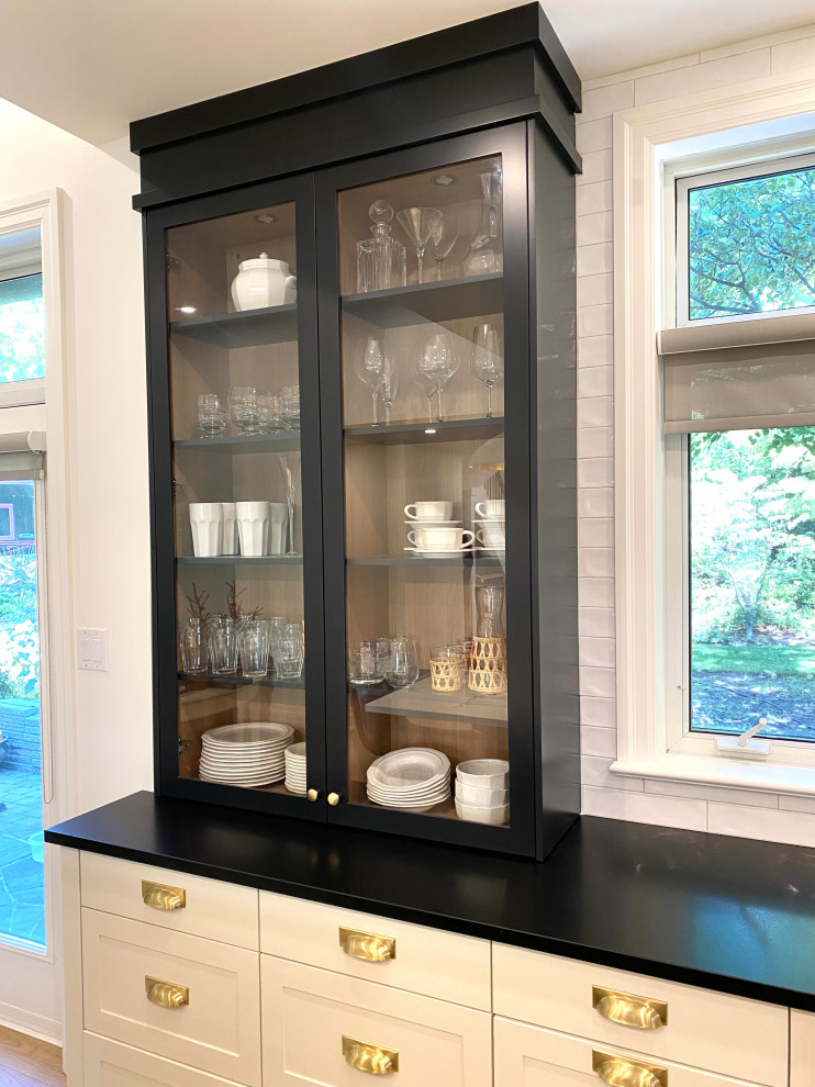 Inspiration for a mid-sized transitional l-shaped light wood floor open concept kitchen remodel in Toronto with a farmhouse sink, shaker cabinets, white cabinets, quartz countertops, white backsplash, porcelain backsplash, an island and black countertops