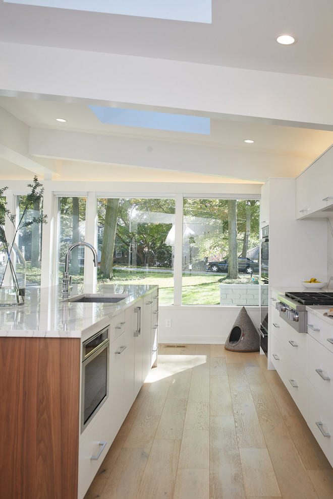 Large modern galley eat-in kitchen in Los Angeles with flat-panel cabinets, medium wood cabinets, quartz benchtops, mirror splashback, stainless steel appliances, light hardwood floors, with island, white floor and white benchtop.