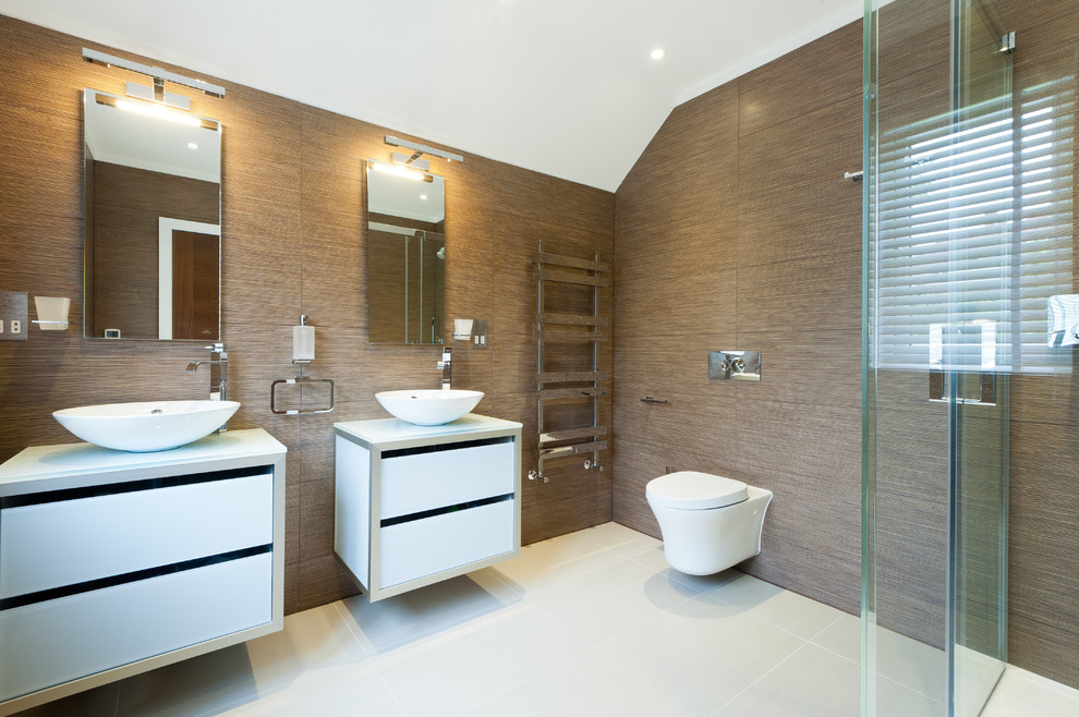 This is an example of a contemporary bathroom in London with a vessel sink, flat-panel cabinets, white cabinets, a corner shower, a wall-mount toilet and brown walls.