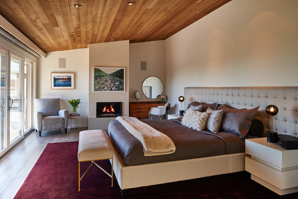 Large midcentury bedroom in Seattle with a standard fireplace, beige walls, medium hardwood floors and a plaster fireplace surround.