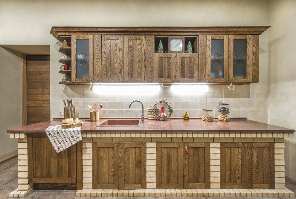 This is an example of a mid-sized country single-wall separate kitchen in Moscow with an integrated sink, raised-panel cabinets, brown cabinets, granite benchtops, beige splashback, ceramic splashback, stainless steel appliances and porcelain floors.