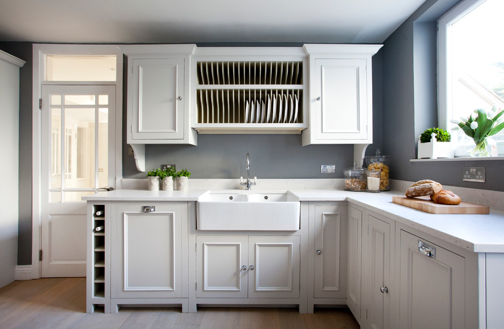 This is an example of a country l-shaped kitchen in Dublin with a farmhouse sink, beaded inset cabinets, grey cabinets and light hardwood floors.